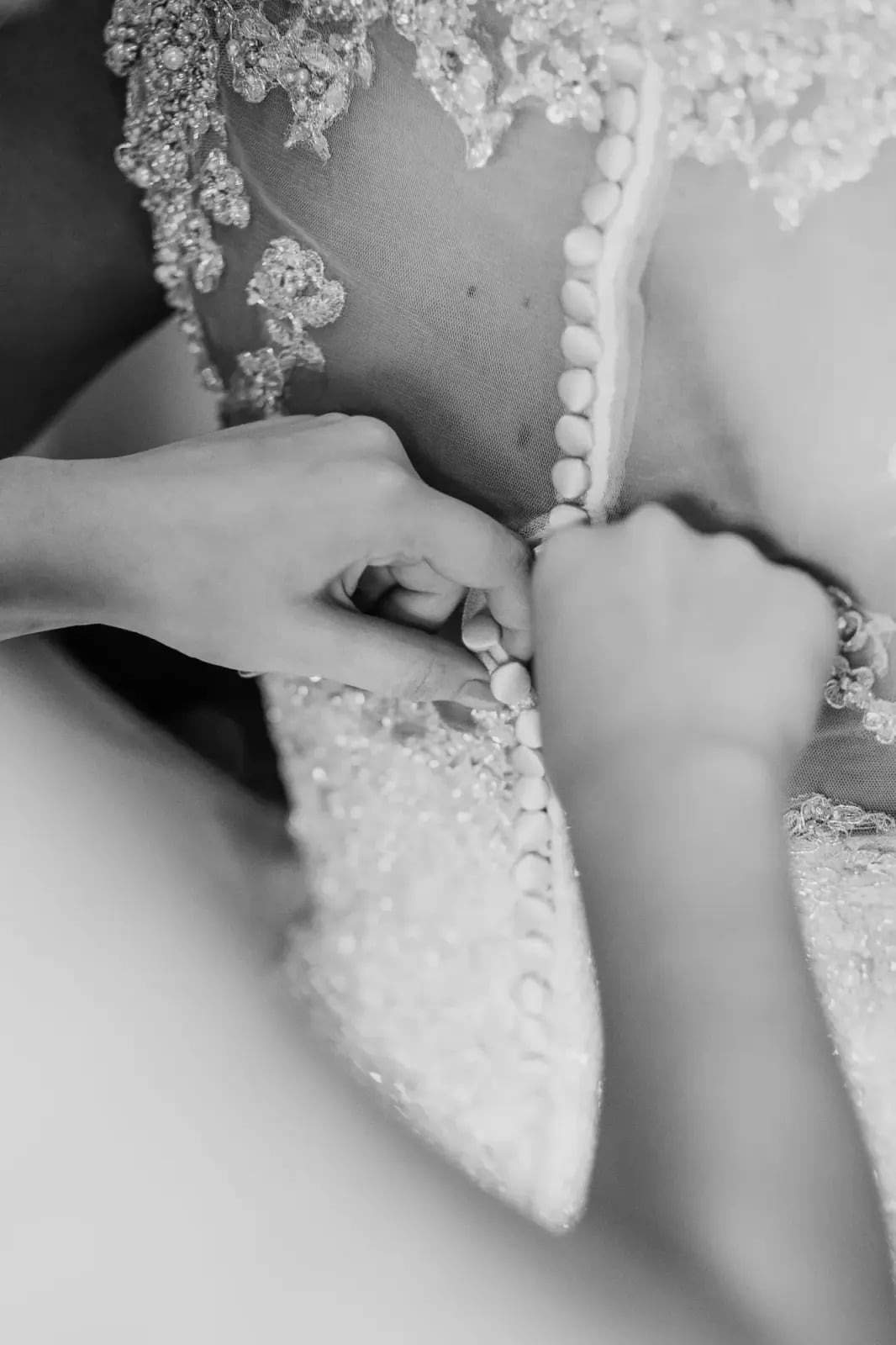 Schwarz-weiß-Foto: Hände schließen die Knopfleiste am Rücken eines Brautkleids